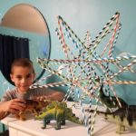 Young boy posing next to a straw star alongside a collection of toy dinosaurs